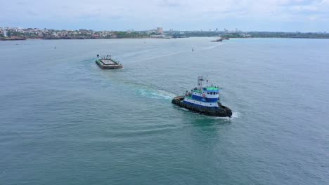 Tugboat-drags-platform-out-of-harbor-in-open-sea-with-city-in-background