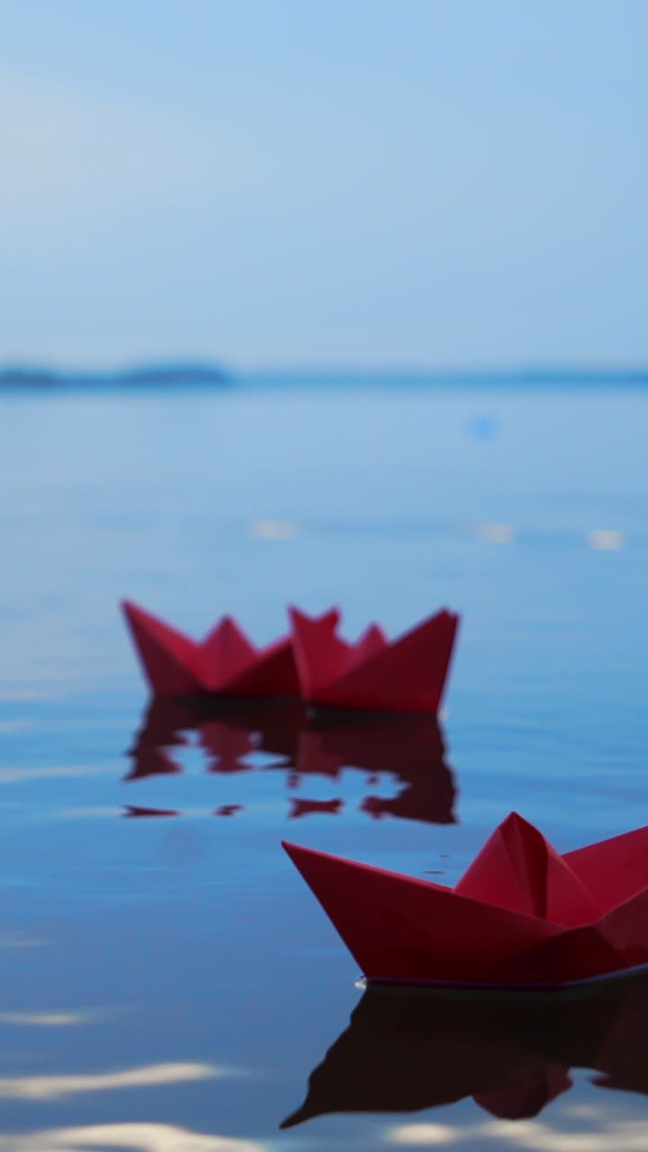 Childish paper boats floating on the water surface on the blurred background. Three red homemade ships on the river Vertical video