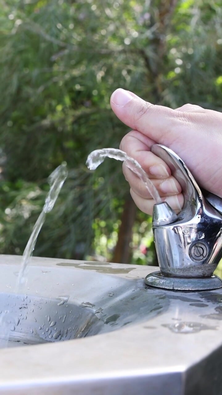 Una mano preme ripetutamente un pulsante in acciaio inossidabile, rilasciando un getto d'acqua fresca.