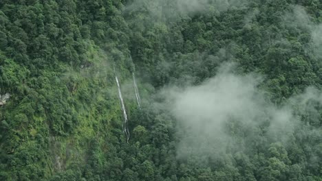 aerial view of waterfall in clouds in mountain forest, beautiful green nature shot of elevated aerial view of waterfalls in himalaya mountains in nepal in lush greenery forest scenery