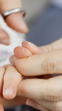 a vertical close-up of a parent gently cutting a toddler’s fingernails, showing care and precision in a quiet moment.