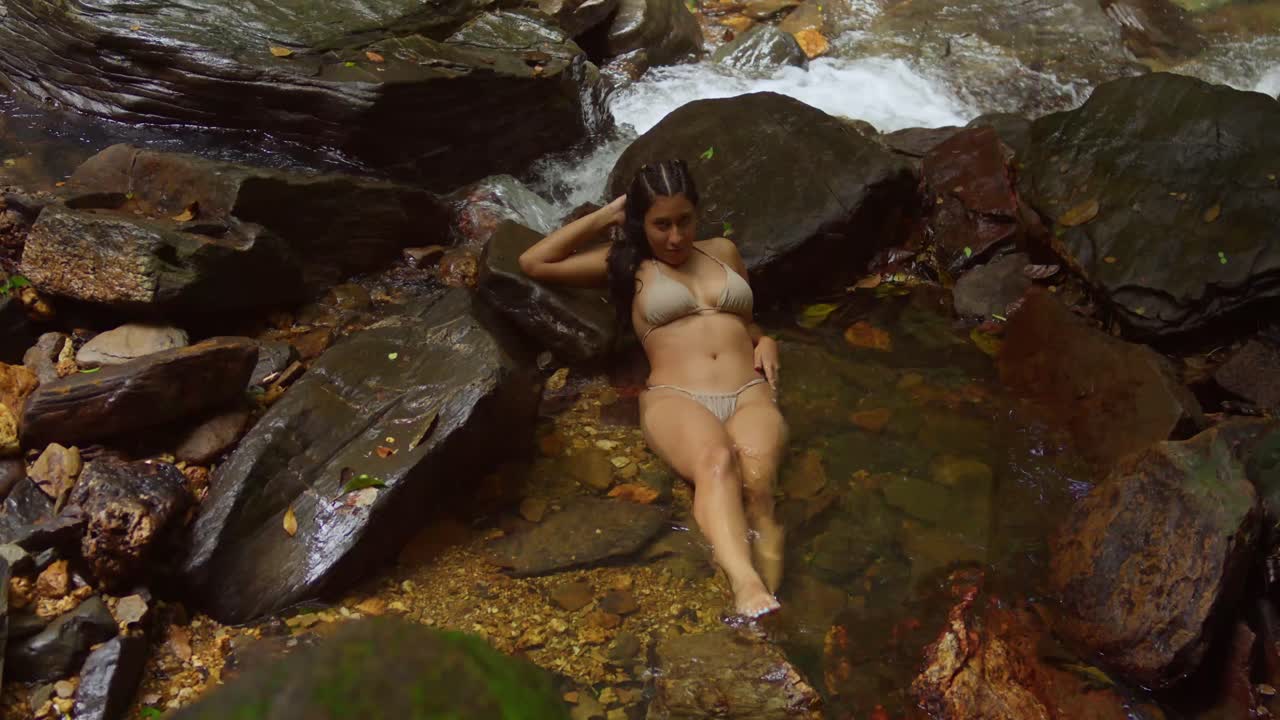La luce del sole filtra attraverso la chioma degli alberi, illuminando una giovane ragazza latina in piedi accanto alla piscina cristallina della cascata Avocat