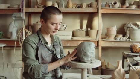 female artist sculpting clay head in workshop