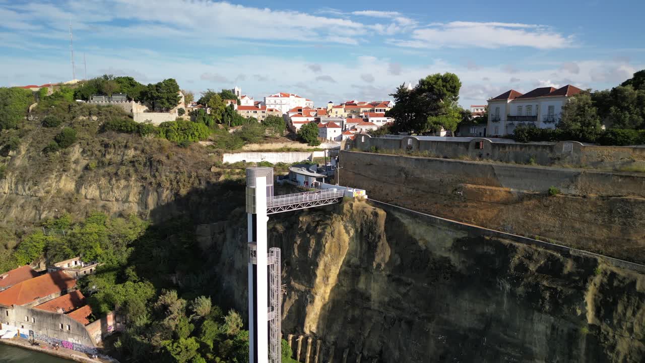 Drone video captures Nazaré's iconic lift on lush cliffs, connecting whitewashed Sitio district to the Atlantic. Bright terracotta roofs under serene daylight complete the scenic spectacle