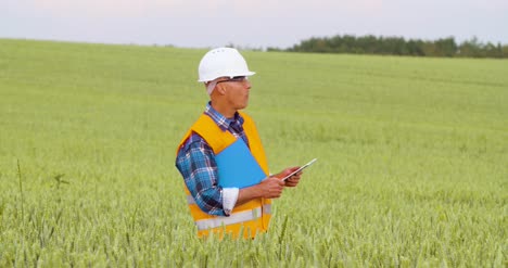 Engineer-Analyzing-Traffic-Polution-On-Clipboard-Amidst-Crops-At-Farm