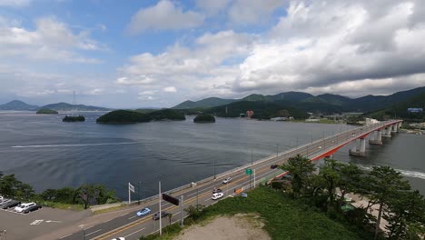 aerial view of traffic at geoje-daegyo bridge with boats sailing across geojedo island in south korea