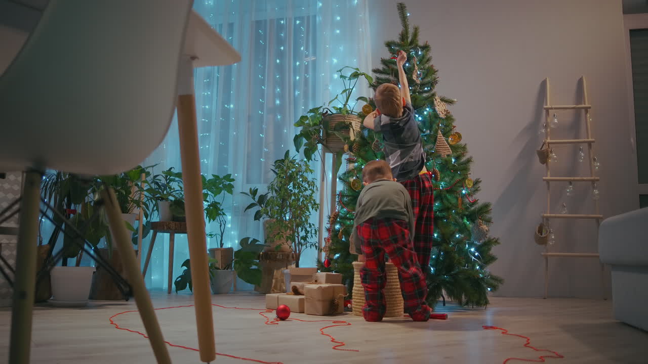 dos hermanos en pijama decoran el baile de navidad en la sala de estar de la casa en la víspera de navidad. imágenes de alta calidad 4k