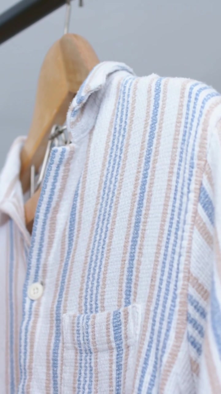 Video verticale: Mano che scorre tirando una camicia a righe su un appendiabiti, scegliendo un capo tra gli appendiabiti, top rosa