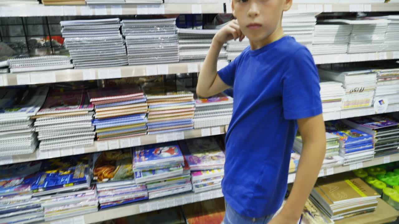 Vinnitsa, Ukraine - August, 2018: Cute child choosing school stationery in store. Many colorful tools and supplies on the shelf of a stationery shop