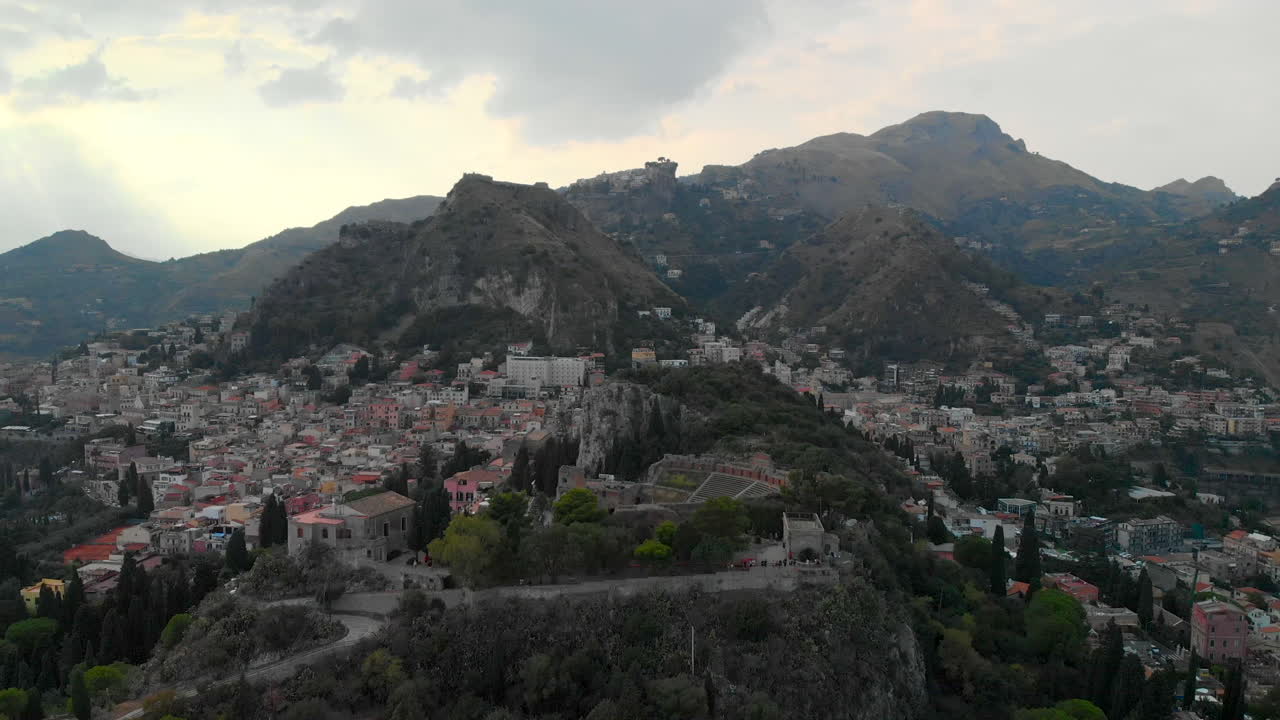 AERIAL DOLLY IN: Drone descending above the ancient theatre of Taormina Sicily, with a spectacular view of the old Italian villages on top of the mountains