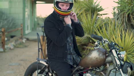 man gears up with helmet and jacket before taking off on vintage chopper motorcycle in the desert