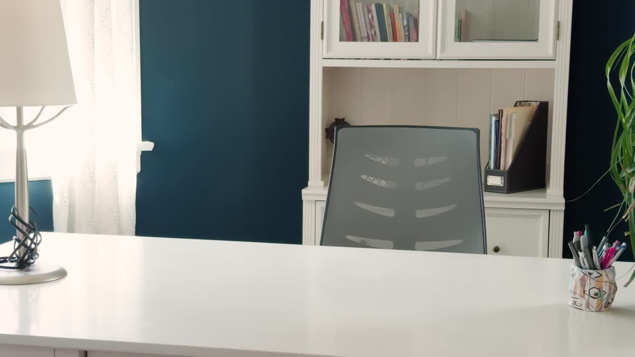 Left to right glide reveals clean home office desk with chair, lamp and bookshelf