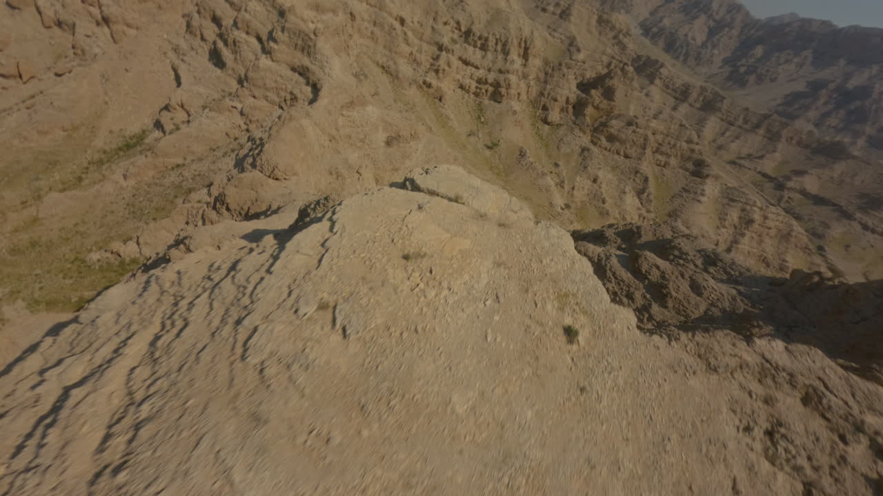 FPV drone descends from the top of a rocky mountain in Hatta Desert, flying close to the cliffs and following the rugged rock formations with smooth, controlled motion