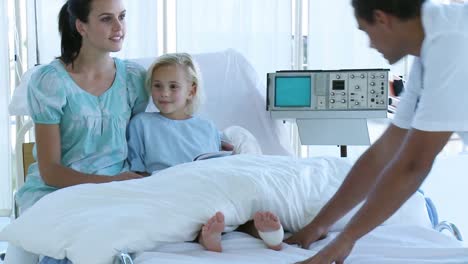 doctor bandaging a little girls foot in bed with her mother