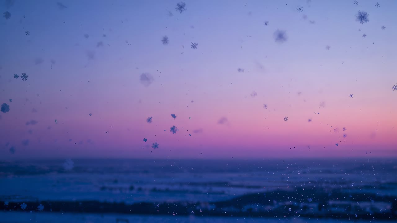 Drifting nearby snowflakes on glass pane being moved by cold dawn breeze, revealing coastal horizon