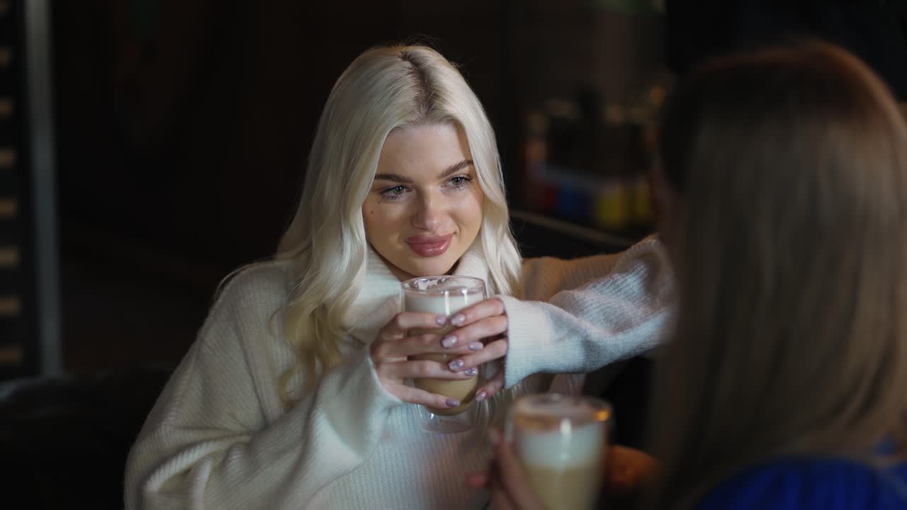 Beautiful long-haired blonde girl is chatting with her friend over a cup of cappuccino at the cafe
