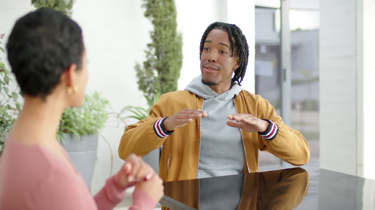 African American man leaning forward explaining with rising palms beside peer at table on terrace
