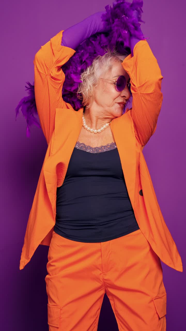 Donna anziana energica che balla con boa di piume su sfondo viola