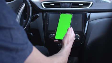 un conductor masculino usa un teléfono inteligente verticalmente con una pantalla verde, sostiene un teléfono en la mano. maqueta para un navegador o aplicación de carretera. desliza a la izquierda o a la derecha con el dedo. desplaza a través de fotos.