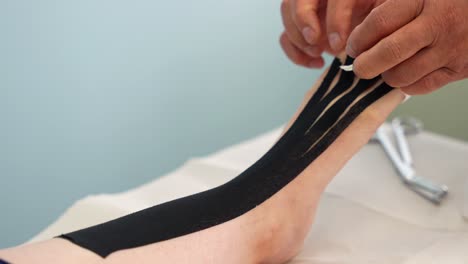 physiotherapist hands placing kinesio tape on patient shin, instep and toes