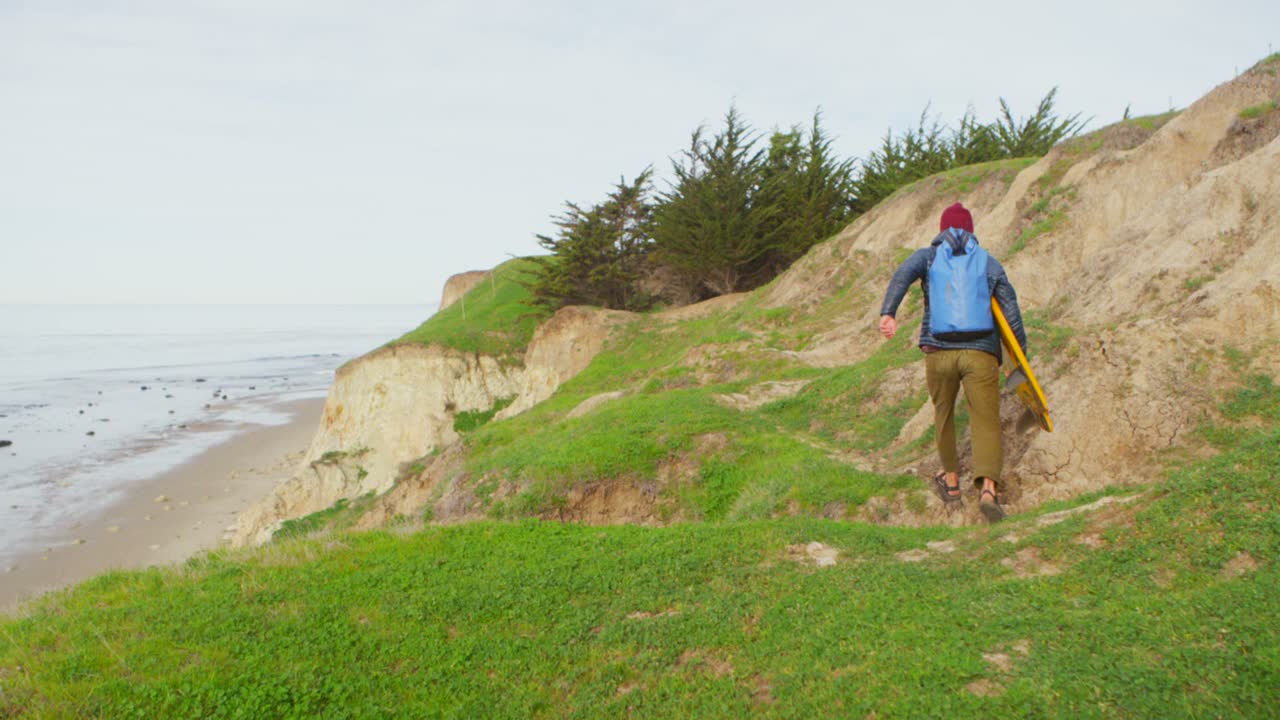un surfista corre hacia la playa después de una larga caminata hasta un punto de surf remoto