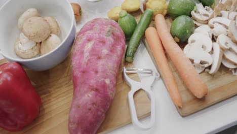 hands of biracial woman preparing an assortment of vegetables on kitchen countertop, slow motion