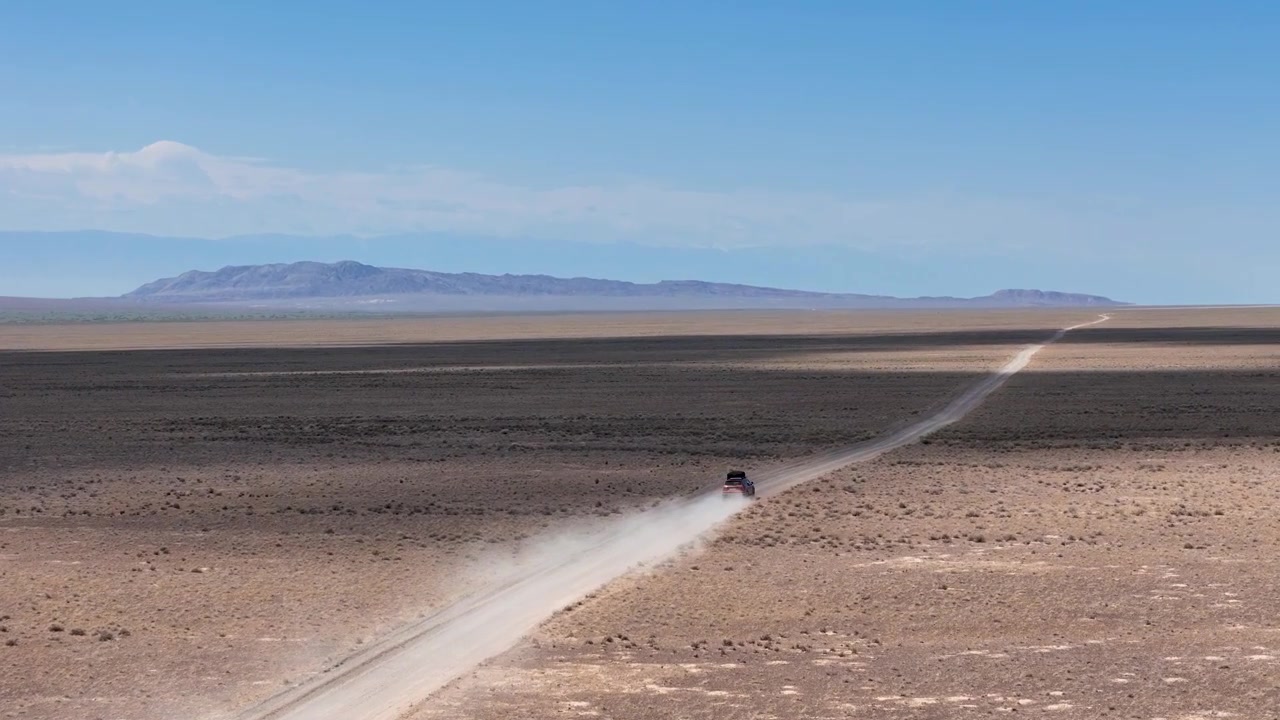Un'auto che guida su una strada remota sollevando polvere nel Parco Nazionale Altyn Emel del Kazakistan