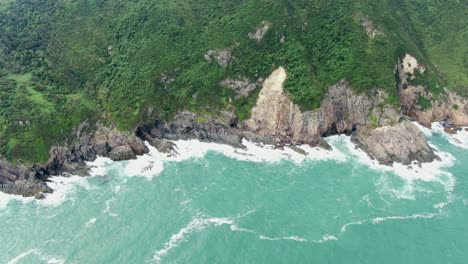 Aerial-view-of-a-jagged-rock-island,-surrounded-with-lush-green-nature-and-Hong-Kong-bay-water