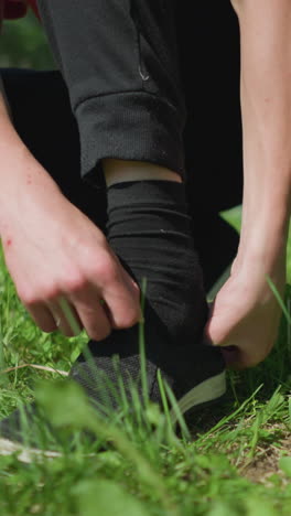 primer plano de alguien ajustando y usando sus zapatos mientras está arrodillado en un campo cubierto de hierba, con otra persona visible moviéndose en el fondo
