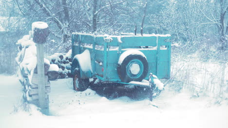 old wood trailer with chipped blue paint surrounded by snow covered chopped wood and tree in distance during a heavy snow