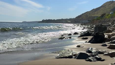 waves-crashing-on-rocky-coast-of-Malibu-coastline-with-sun-reflecting-on-the-water-in-California