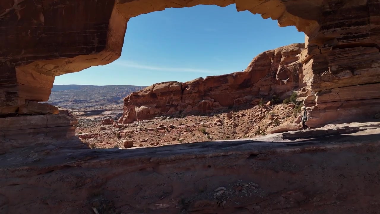 Jeep Arch, Utah USA. Ripresa aerea con drone che rivela il monumento naturale e un'escursionista che cammina sotto, vista in allontanamento