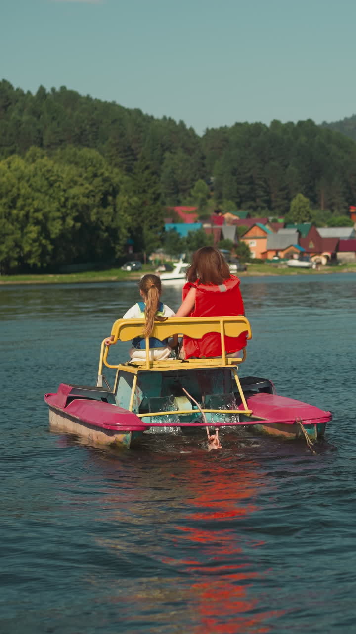 Young mother and little child ride catamaran on lake. Family vacation at reservoir slow motion. Active entertainment on warm summer day backside view