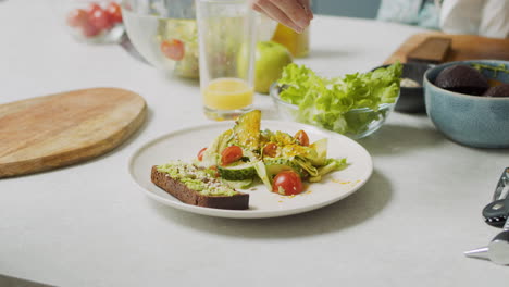 primer plano de la mano de una mujer agregando varias semillas en un plato con ensalada fresca y tostadas de aguacate 1