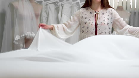 Clothing-designer-is-working-with-measurements-on-a-studio-table.-Shot-on-in-4K-UHD-.-Closeup-deploy-a-skein-of-white-fabric-in-white-and-light-colored-sewing-in-slow-motion.-handmade-tailoring-of-exclusive-wedding-dresses