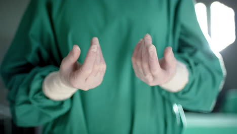 midsection of caucasian male surgeon wearing medical gloves in operating theatre, slow motion