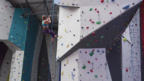 Caucasian-woman-wearing-face-mask-climbing-wall-at-indoor-climbing-wall