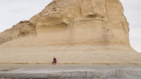 Young-Male-Model-Sitting-Near-A-Sandstone-Cliff-During-Sunset---Very-Wide-Shot