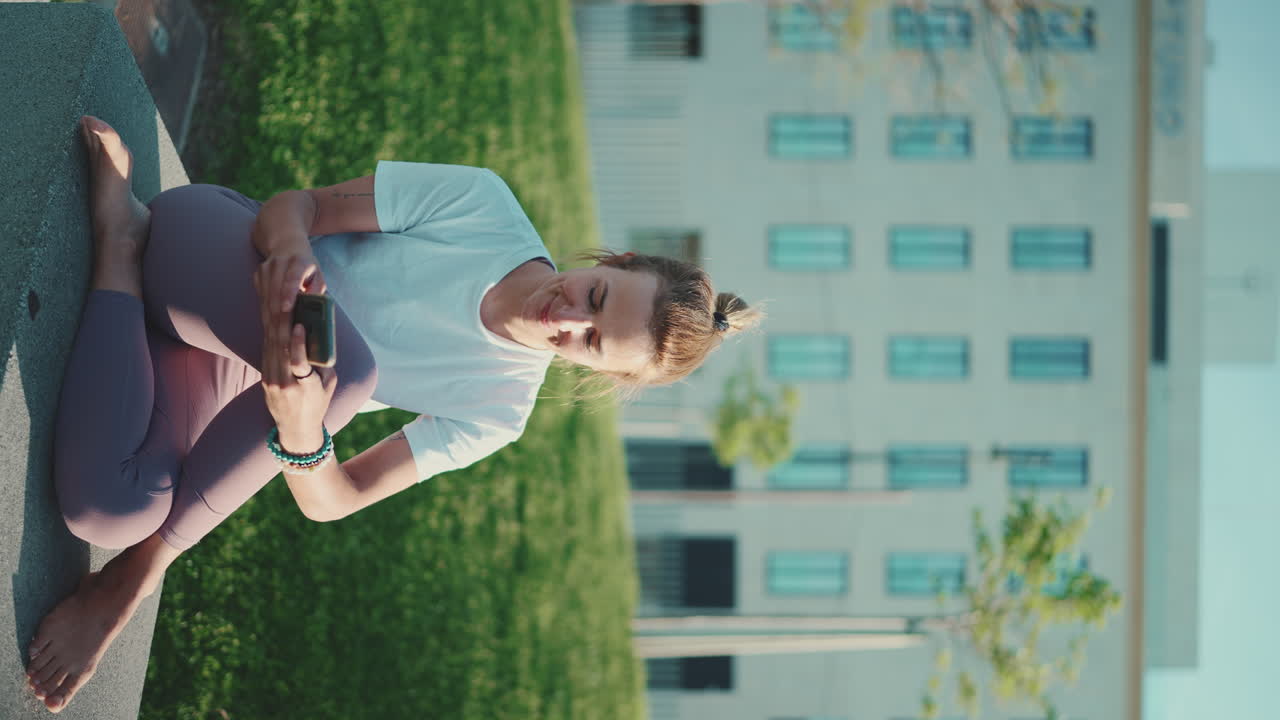 스포츠 옷을 입은 백인 여성이 밖에서 스마트폰을 확인하고 있습니다.