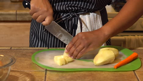 mujer negra cortando papas en una tabla de cortar de silicona en la cocina, cerrada