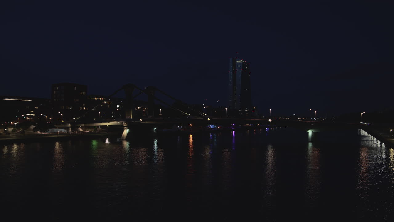 Night view of Frankfurt’s skyline featuring the European Central Bank and colorful lights reflecting in the river. Dark moody scene with urban atmosphere