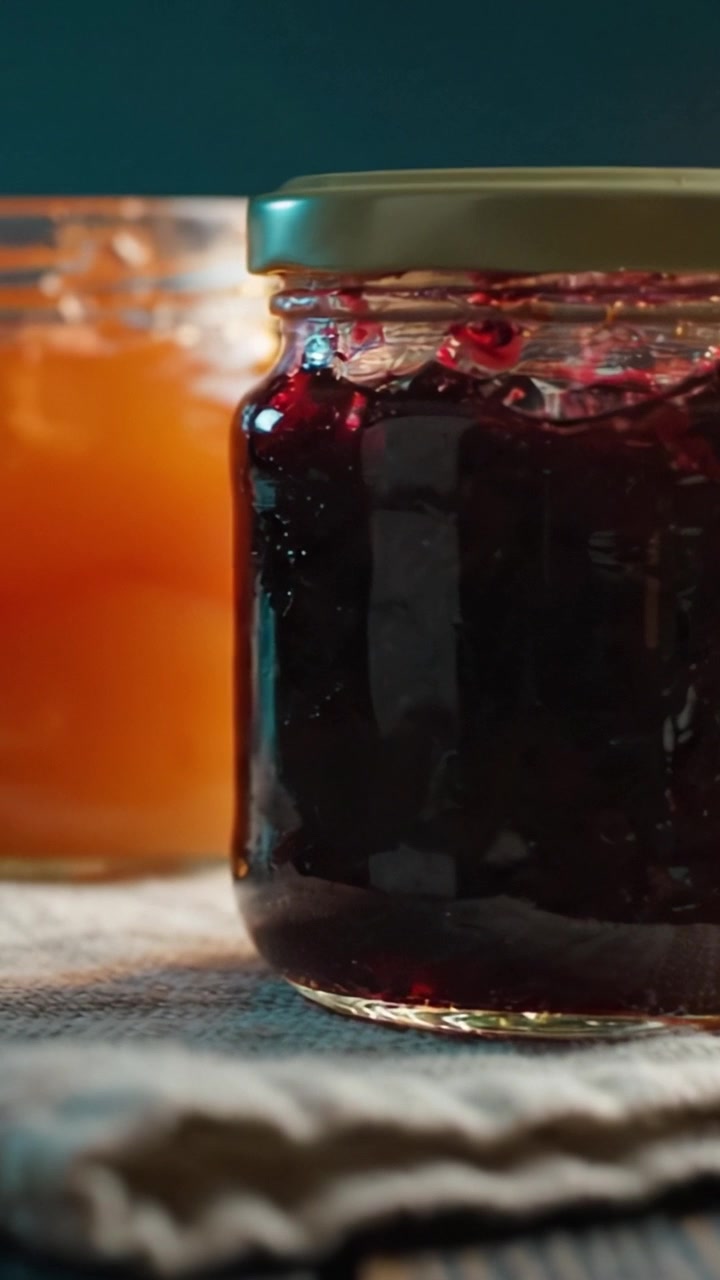 A Close-Up View of Two Glass Jars Containing Delicious Homemade Preserves, Featuring a Dark Berry Jam and a Golden Fruit Preserve on a Rustic Tabletop