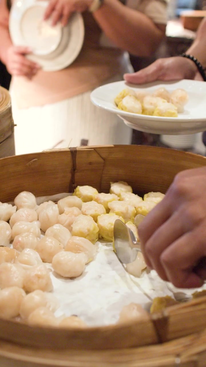 Primo piano di una persona che seleziona ravioli shumai da un grande cestello di bambù per la cottura a vapore