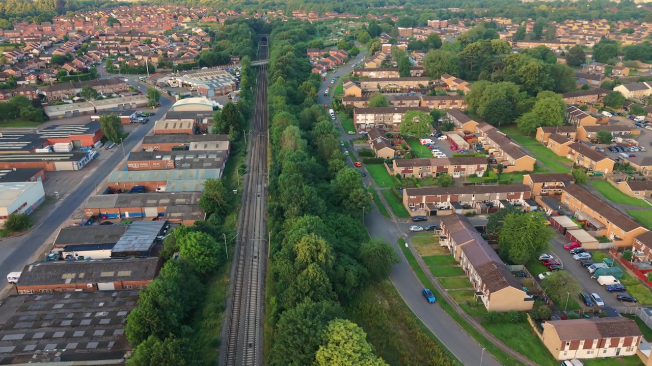 Riprese aeree catturano un quartiere residenziale a Northampton, Regno Unito, con binari ferroviari circondati da vegetazione e case, e strutture industriali nelle vicinanze.