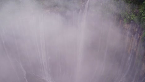 Soaring-through-mist-cloud-revealing-Thousand-Waterfalls-Tumpak-Sewu,-aerial