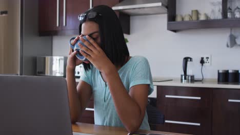 persona de género mixto fluida sentada en un escritorio bebiendo café trabajando desde casa usando una computadora portátil