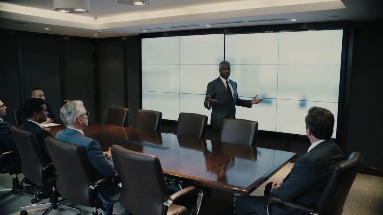 Starting briefing, standing executive in dark suit presenting at boardroom table