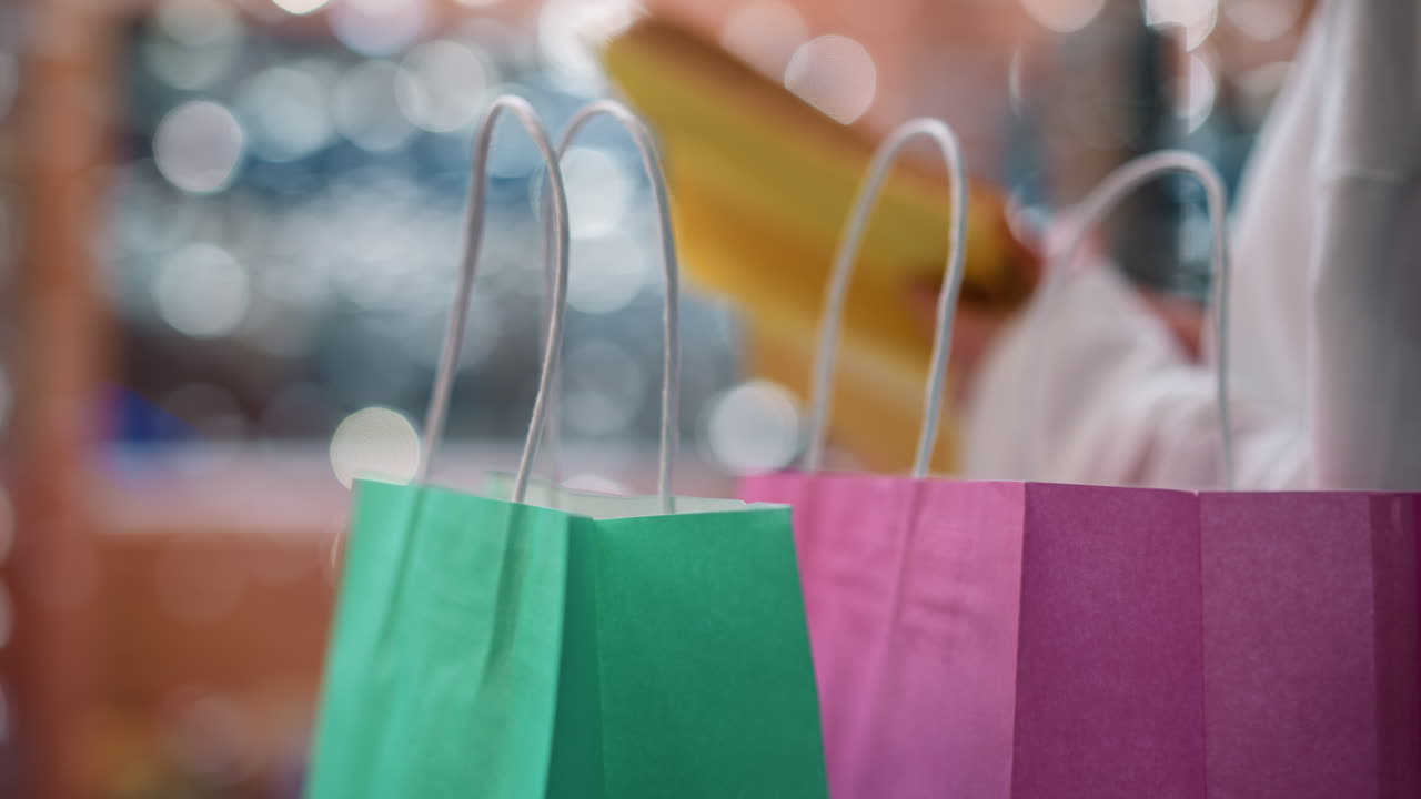 primer plano de bolsas de compras coloridas en primer plano con fondo bokeh borroso, mostrando a una mujer hojeando un libro en un centro comercial