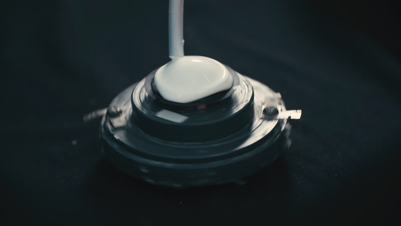 White liquid being dispensed from a nozzle, applied onto a circular speaker component, Industrial part of the assembly process for a speaker driver