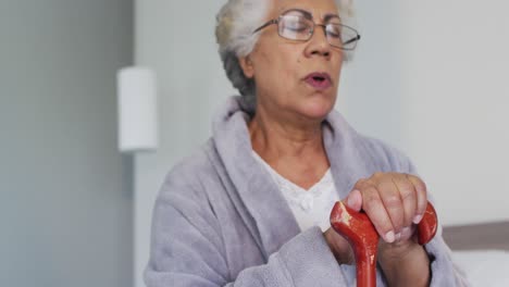 Mujer-Mayor-Afroamericana-Apoyada-En-Su-Bastón-Mientras-Está-Sentada-En-La-Cama-En-Casa